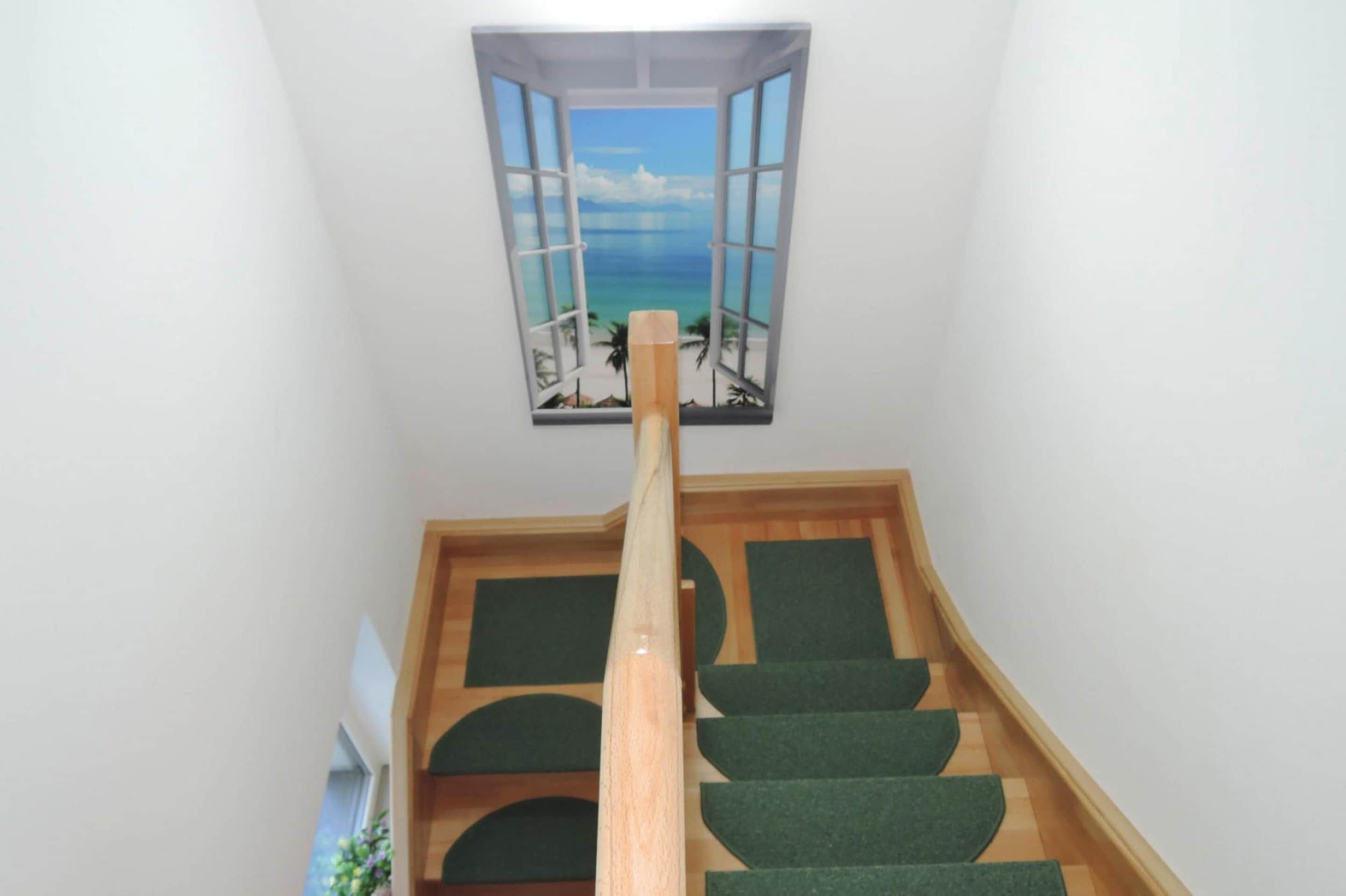 A staircase with a view of a beach through an open window.