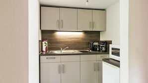 Una cucina compatta dal design moderno, con forno a microonde integrato, macchina del caffè e lavello con rubinetto.