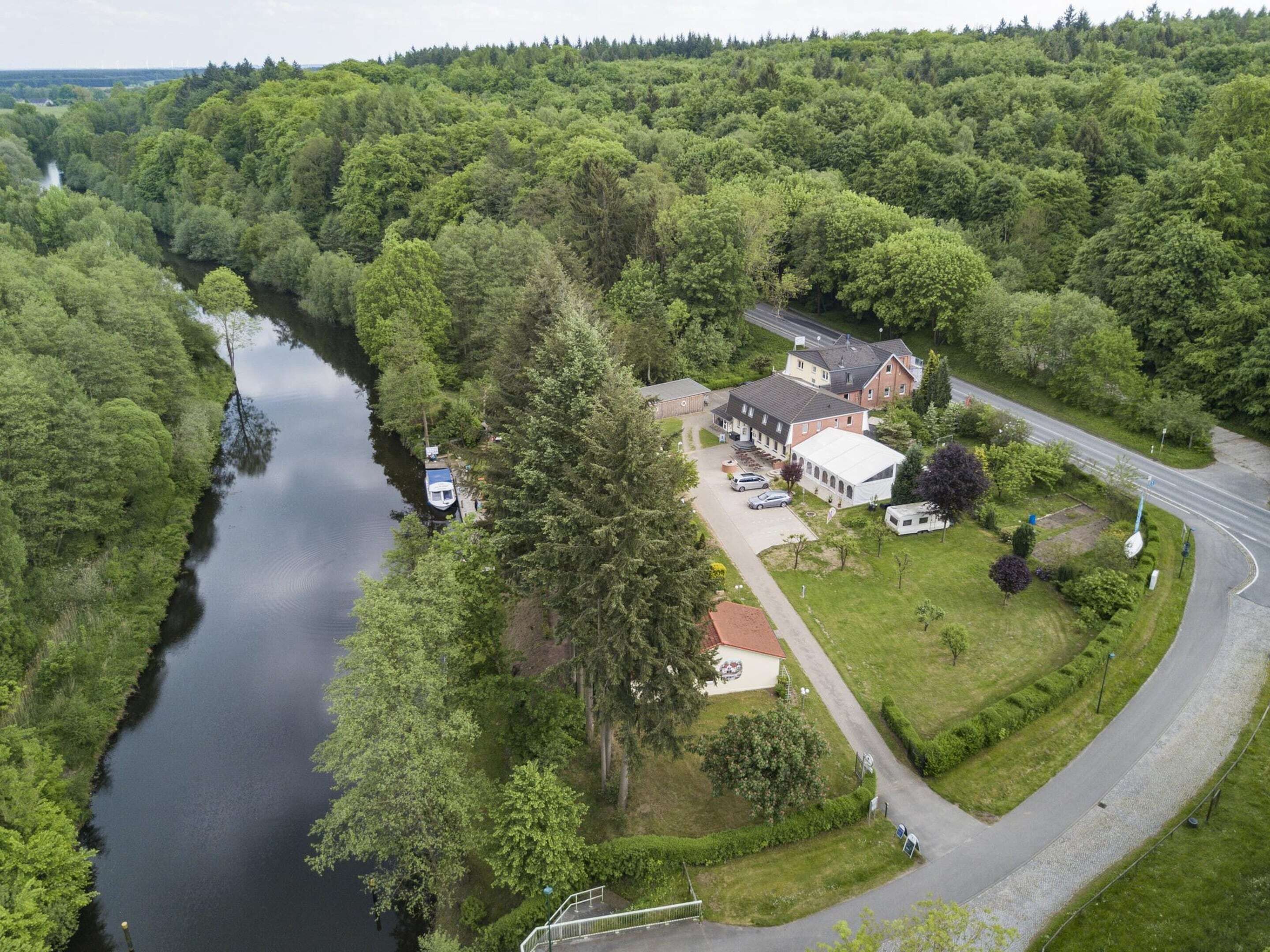 Vue aérienne d’une propriété au bord du lac, avec une maison, un bateau amarré au bord de l’eau et une route qui contourne la propriété.