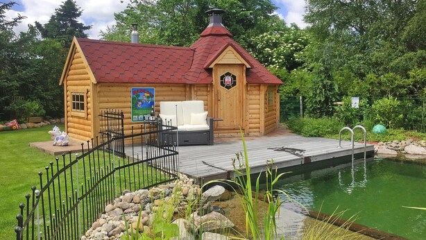 A wooden cabin with a red roof, a deck, and a small pool. - Ferienhaus in Rehm-flehde-bargen mit Gemeinsamer Sauna (Rehm-Flehde-Bargen)