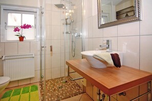 A bathroom with a shower, toilet, sink, and a window with an orchid plant.
