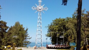 A tall, white metal cross structure in a park with trees and a body of water in the background. - Year-round Holiday House Near the Sea, Pustkowo (Rewal)