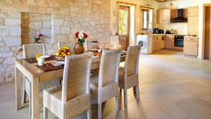 Un coin repas avec des chaises en osier et un mur en pierre, une cuisine équipée d’appareils électroménagers modernes et une cheminée en pierre.