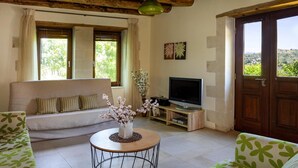 Un salon comprenant un canapé, une table basse avec un vase, un téléviseur et une porte donnant sur l’extérieur.