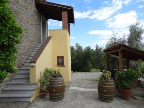 A building with stone walls, a yellow facade, and a wooden staircase. There are potted plants and a pergola in the outdoor area. - Villa in Vinci With Pool & Panoramic Views (Lamporecchio)