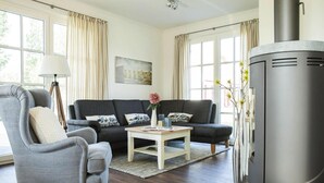 A living room with a sofa, armchair, coffee table, and a fireplace. - Reetdachhaus am Bodden mit Sauna (Fuhlendorf)