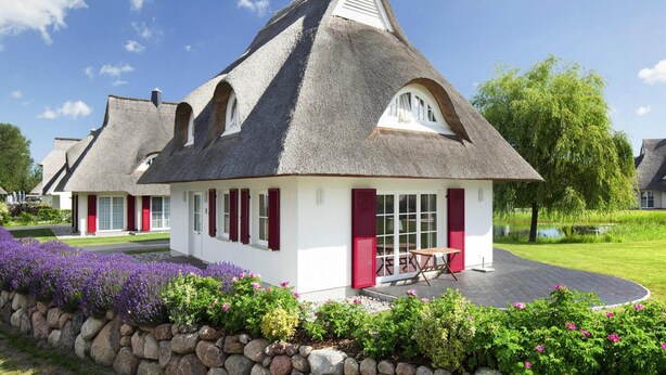 A traditional house with a steeply pitched roof, white walls, and red shutters. - Reetdachhaus am Bodden mit Sauna (Fuhlendorf)