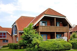A two-story residential building with a red-tiled roof, a wooden balcony, and a brick facade. - Ferienwohnung in Lemkenhafen for 2 Personen (Fehmarn)