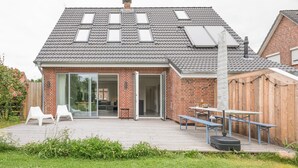 Une maison moderne avec un toit en pente, de grandes portes vitrées et une terrasse en bois.
