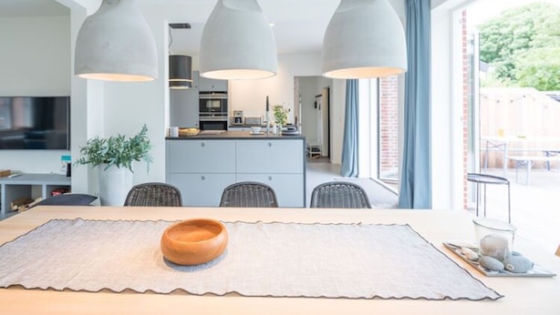 Une cuisine moderne dotée d’un îlot central, d’un éclairage suspendu et d’un coin repas agrémenté d’un centre de table en bois.