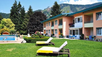 A hotel with a pool, two lounge chairs, and a mountain backdrop.