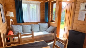 A wooden cabin interior with a sofa, a dining table, chairs, a lamp, and a fireplace. - Holiday Homes Close to the Seaside Beach (Mielno)