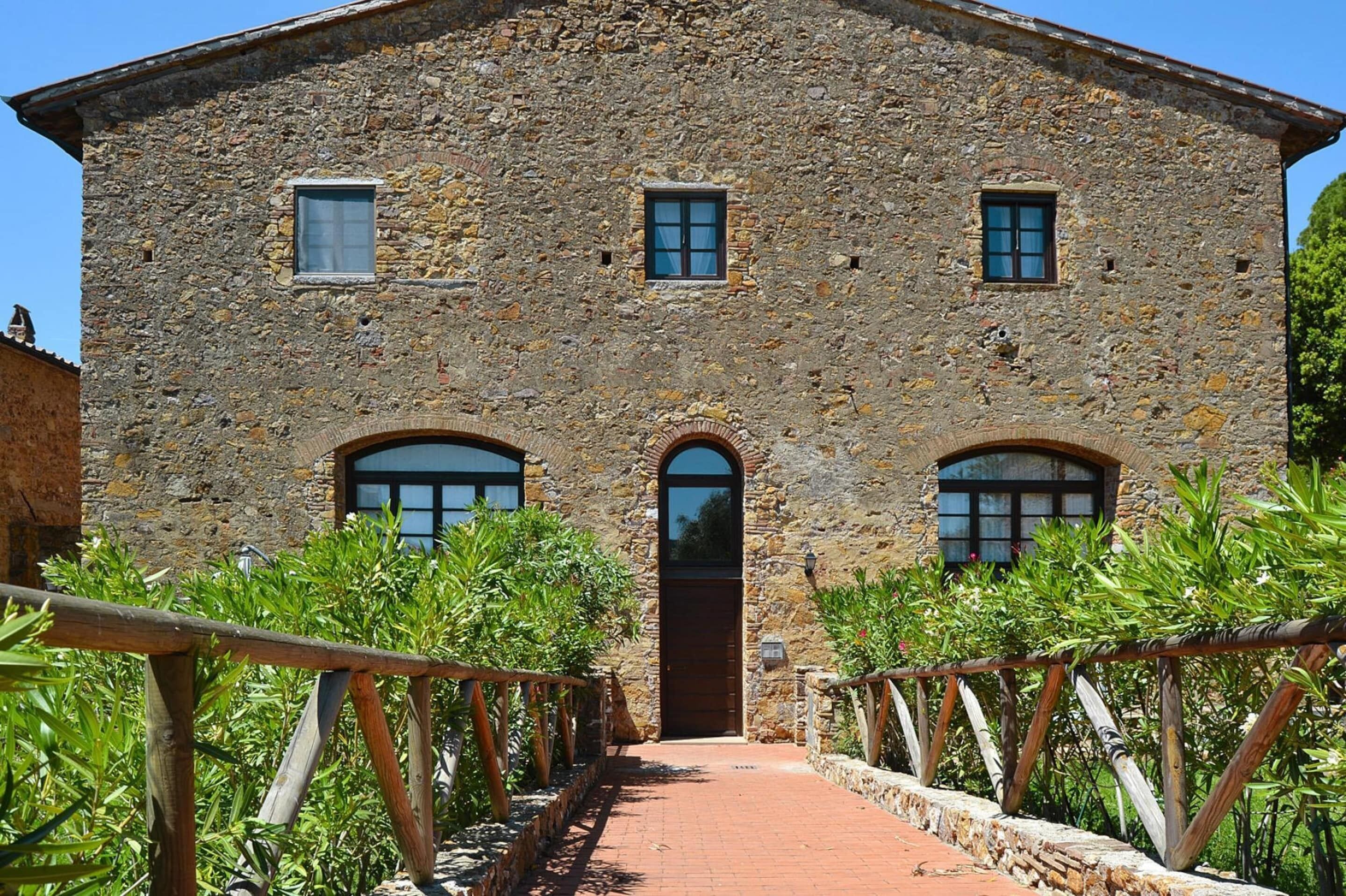 A stone building with a central door, two windows on the upper floor, and a brick pathway leading to it.