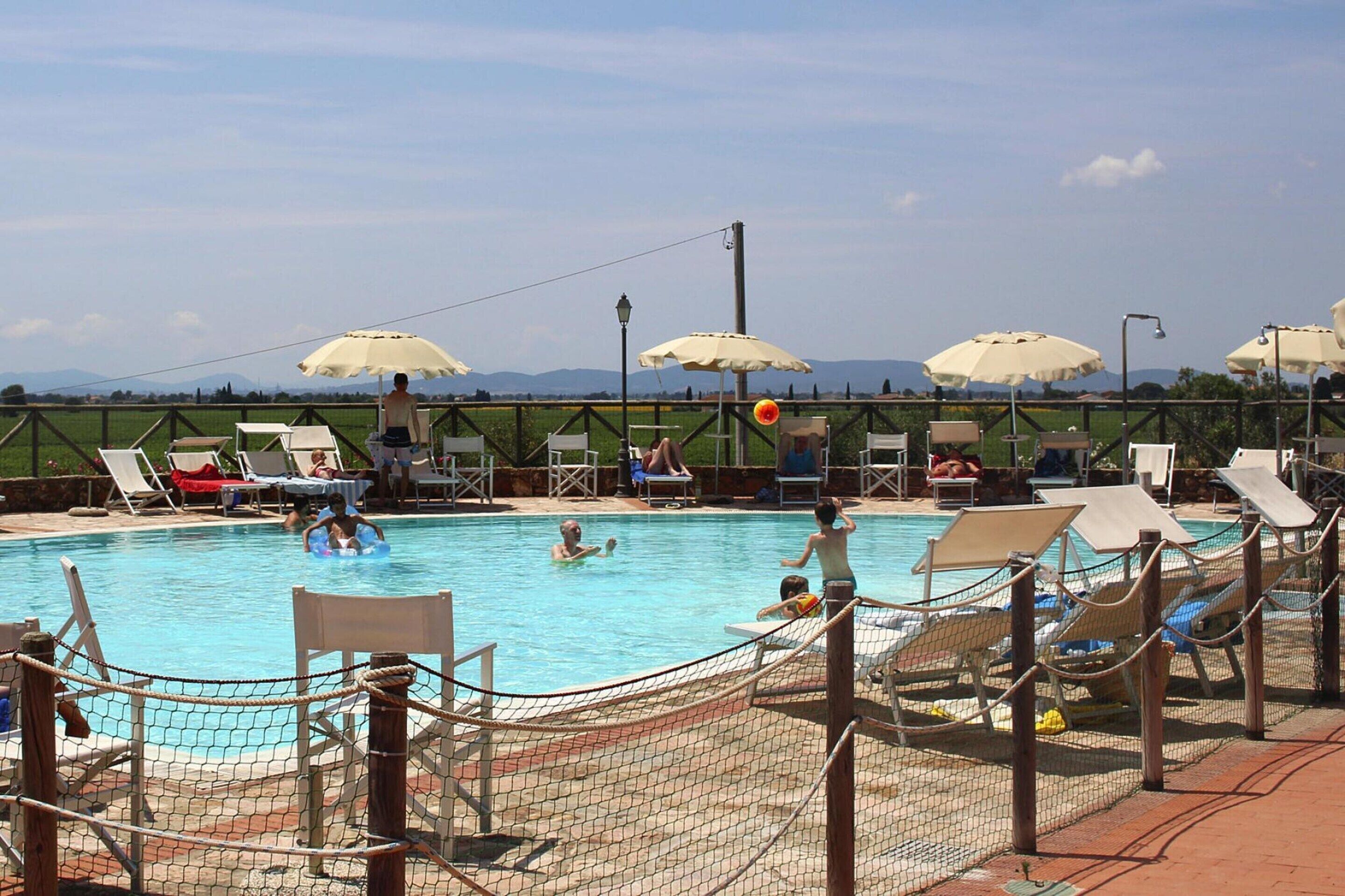 A swimming pool with lounge chairs and umbrellas, surrounded by a fence.