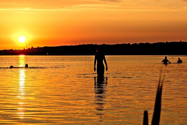 A sunset over a calm body of water with silhouettes of people and a sailboat. - Seepark Auenhain am Markkleeberger See (Markkleeberg)