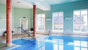 Piscina com água azul cristalina, um pilar vermelho e uma porta com sinalização de saída.