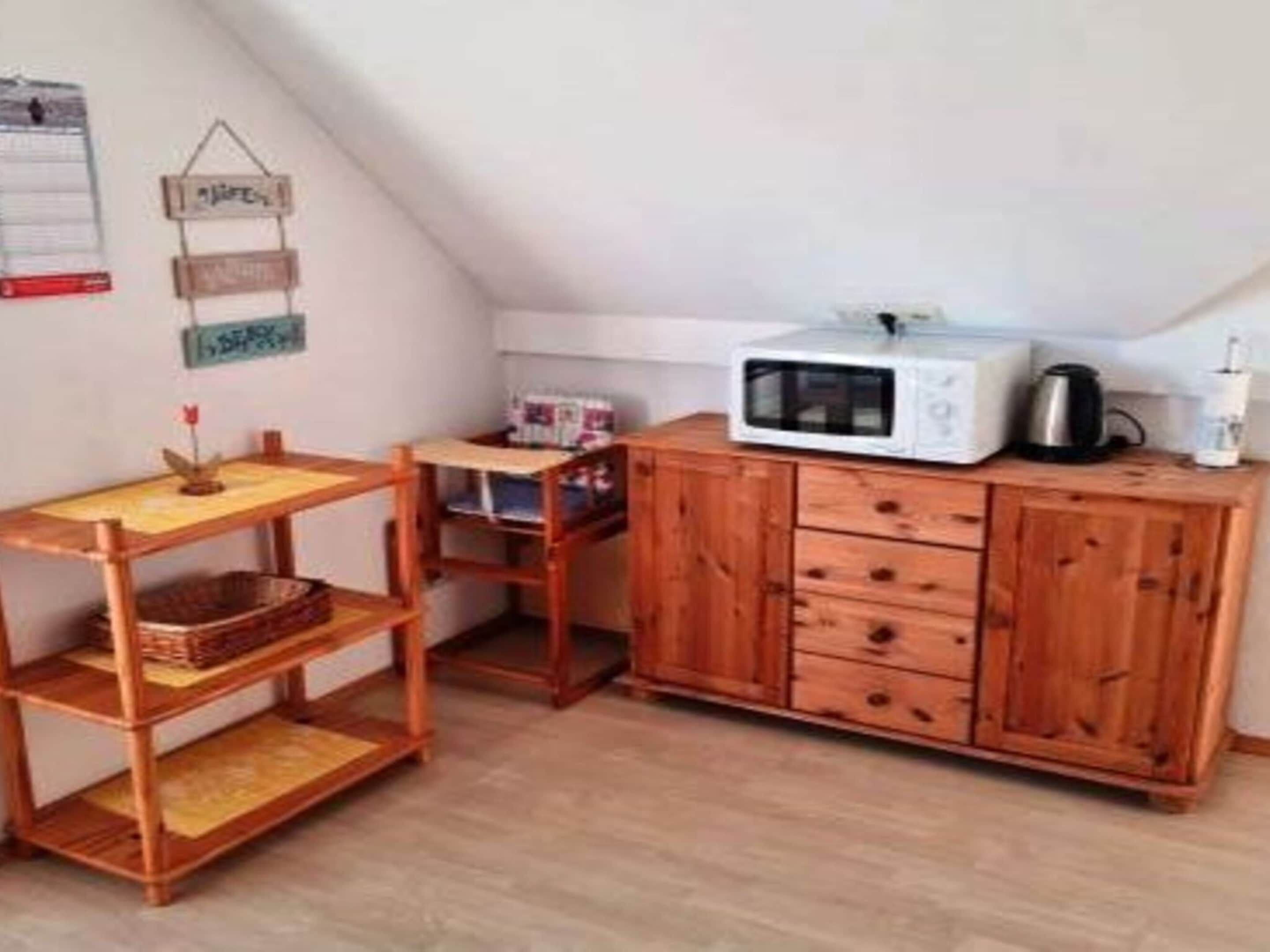 A small kitchenette with a microwave, a kettle, and a wooden cabinet.