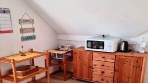 A small kitchenette with a microwave, a kettle, and a wooden cabinet.
