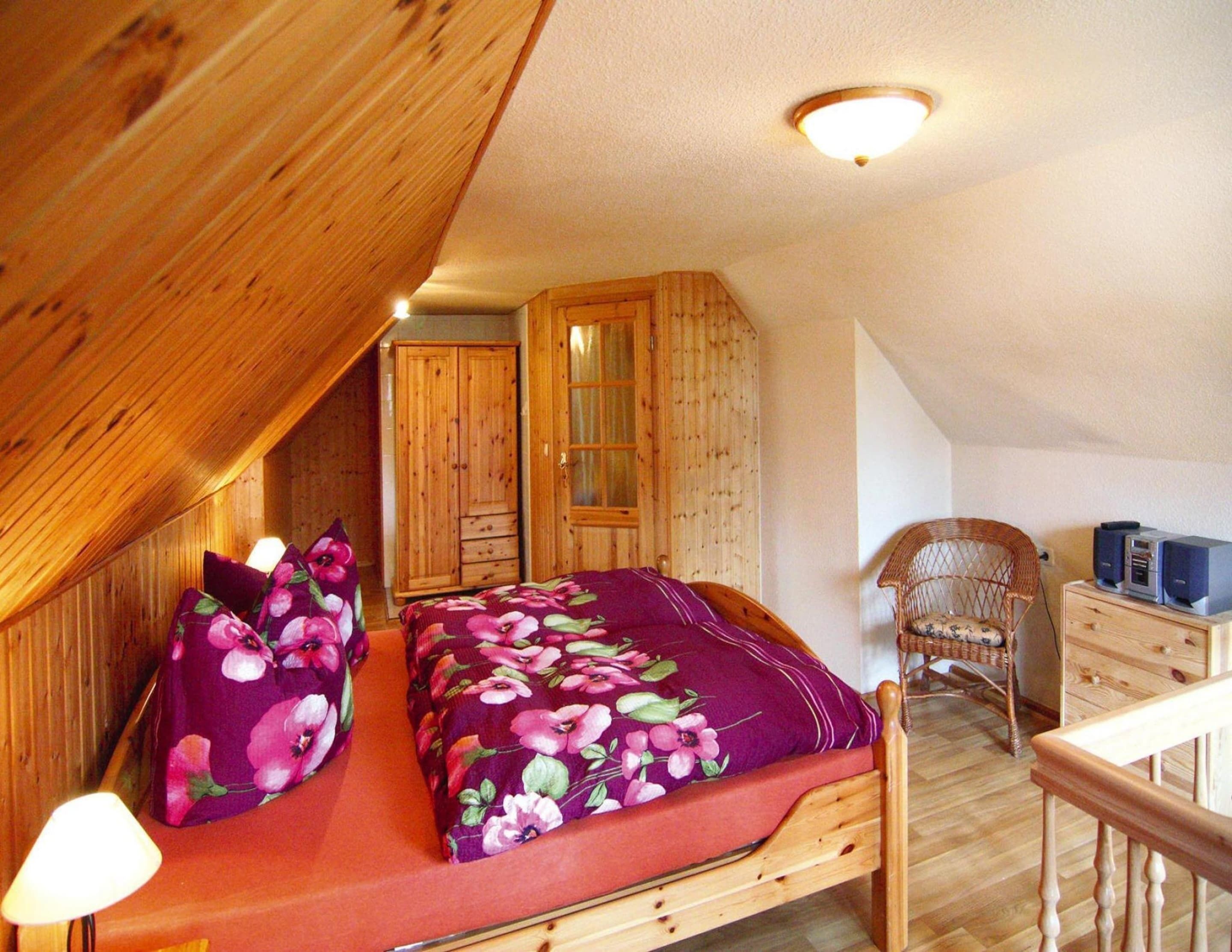 Quarto com cama de madeira, mesa de cabeceira, cadeira e guarda-roupa.