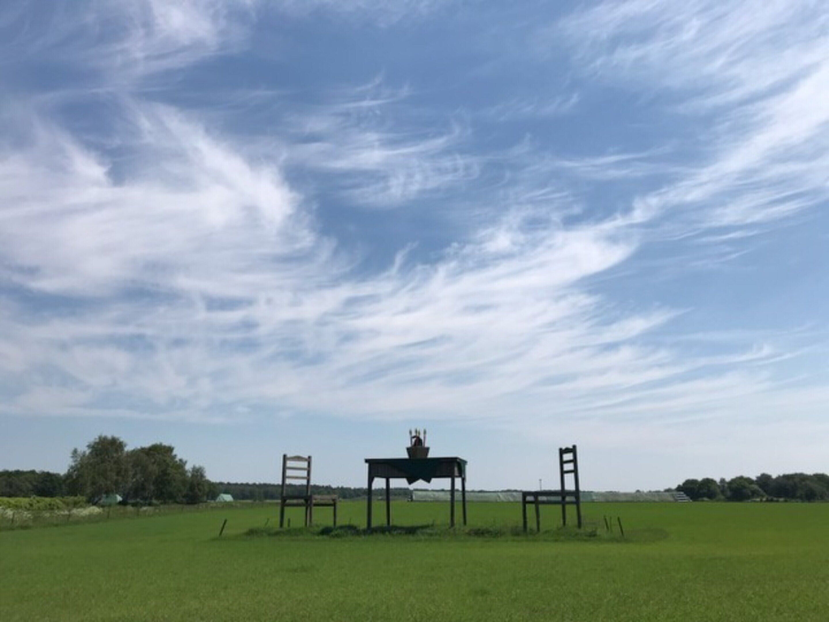 An open field with a table and two chairs under a clear sky.
