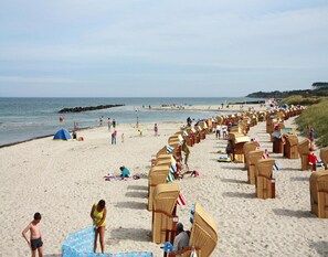 Une plage bordée de rangées de chaises de plage en osier et abritée par une tente.