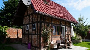 Ein traditionelles Fachwerkhäuschen mit rotem Ziegeldach, einer Satellitenschüssel und einer kleinen Sitzgelegenheit im Freien.