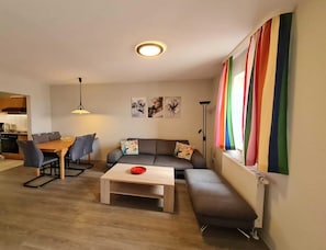 A modern living room with a sofa, coffee table, and dining area. - Wohnung in Orth Nahe Ostsee (Fehmarn)
