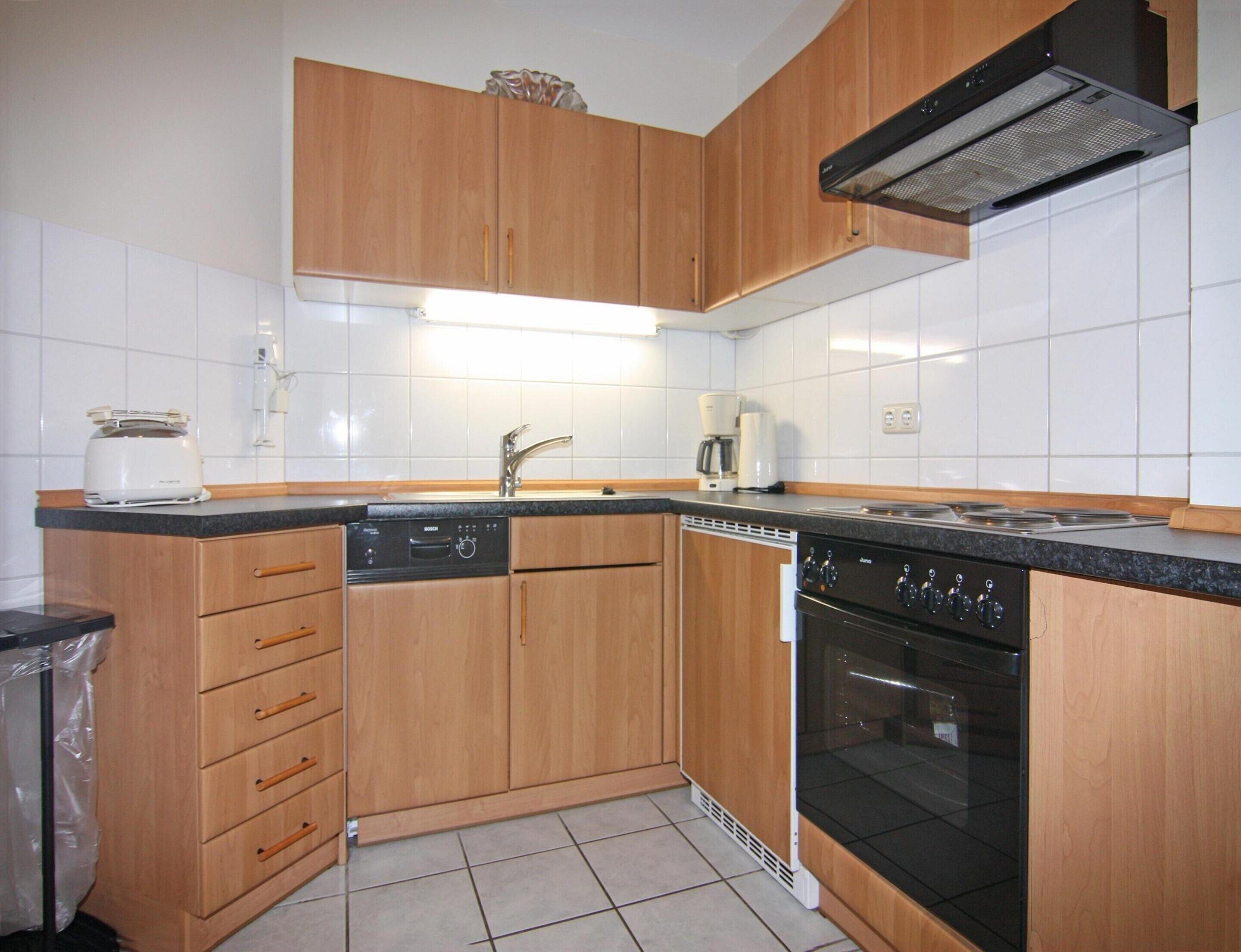 Une cuisine avec des meubles de rangement en bois, un lave-vaisselle, une cuisinière et une machine à café.