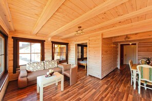 A log cabin interior with a wooden floor, a sofa, a dining table with chairs, and a ceiling with wooden beams. - Comfortable Apartment, 2 Bedrooms, Terrace (Ustronie Morskie)