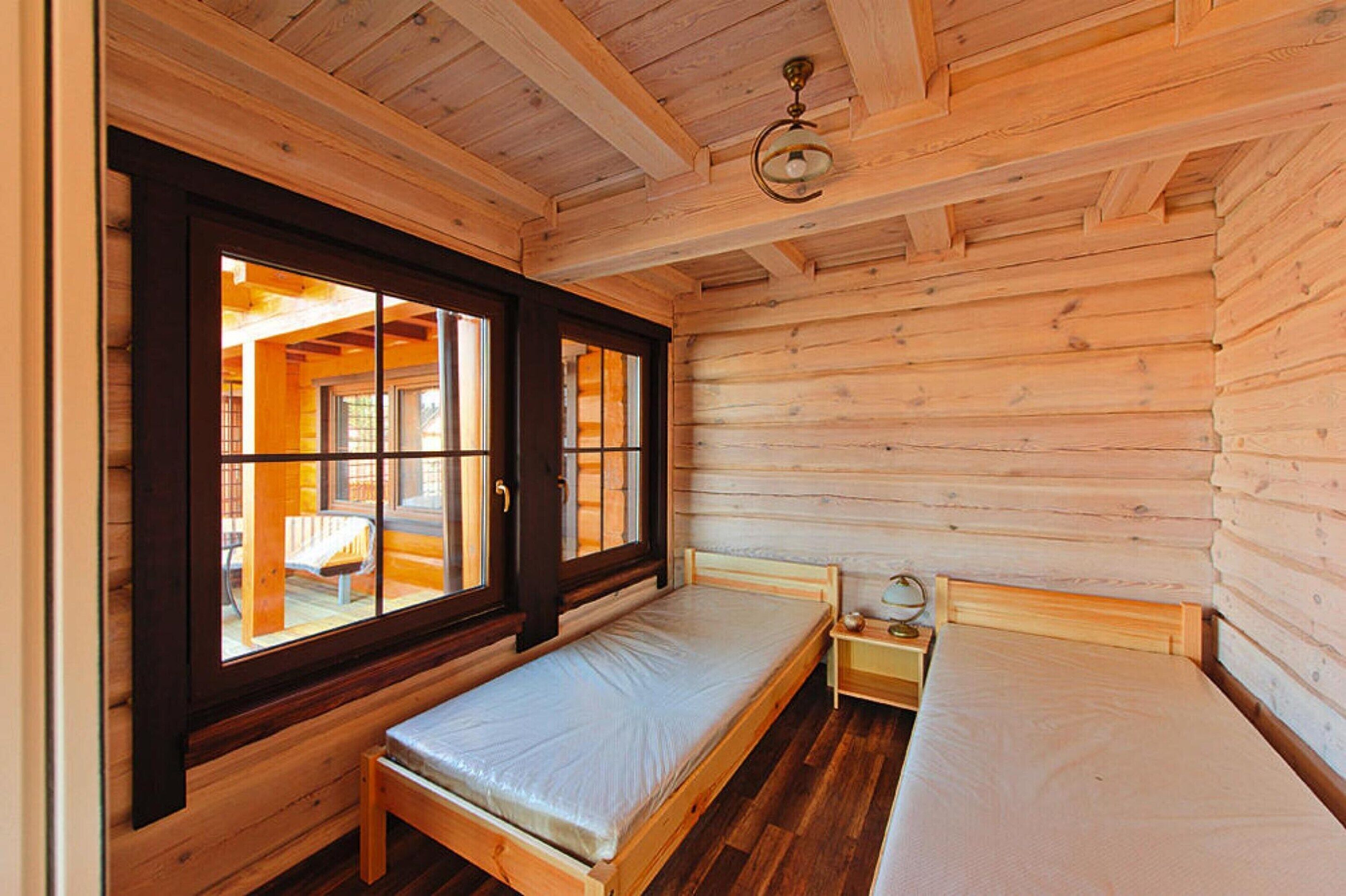 A small wooden cabin room with a single bed, a bench, a small table, and a window with a view of an outdoor area.
