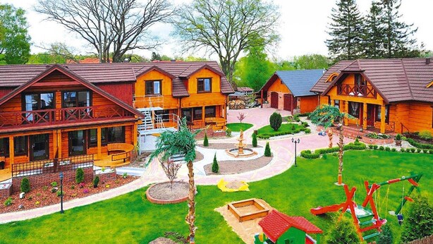 Een lodge met verschillende houten blokhutten, een centrale binnenplaats met een fontein en een omheind speelgedeelte.