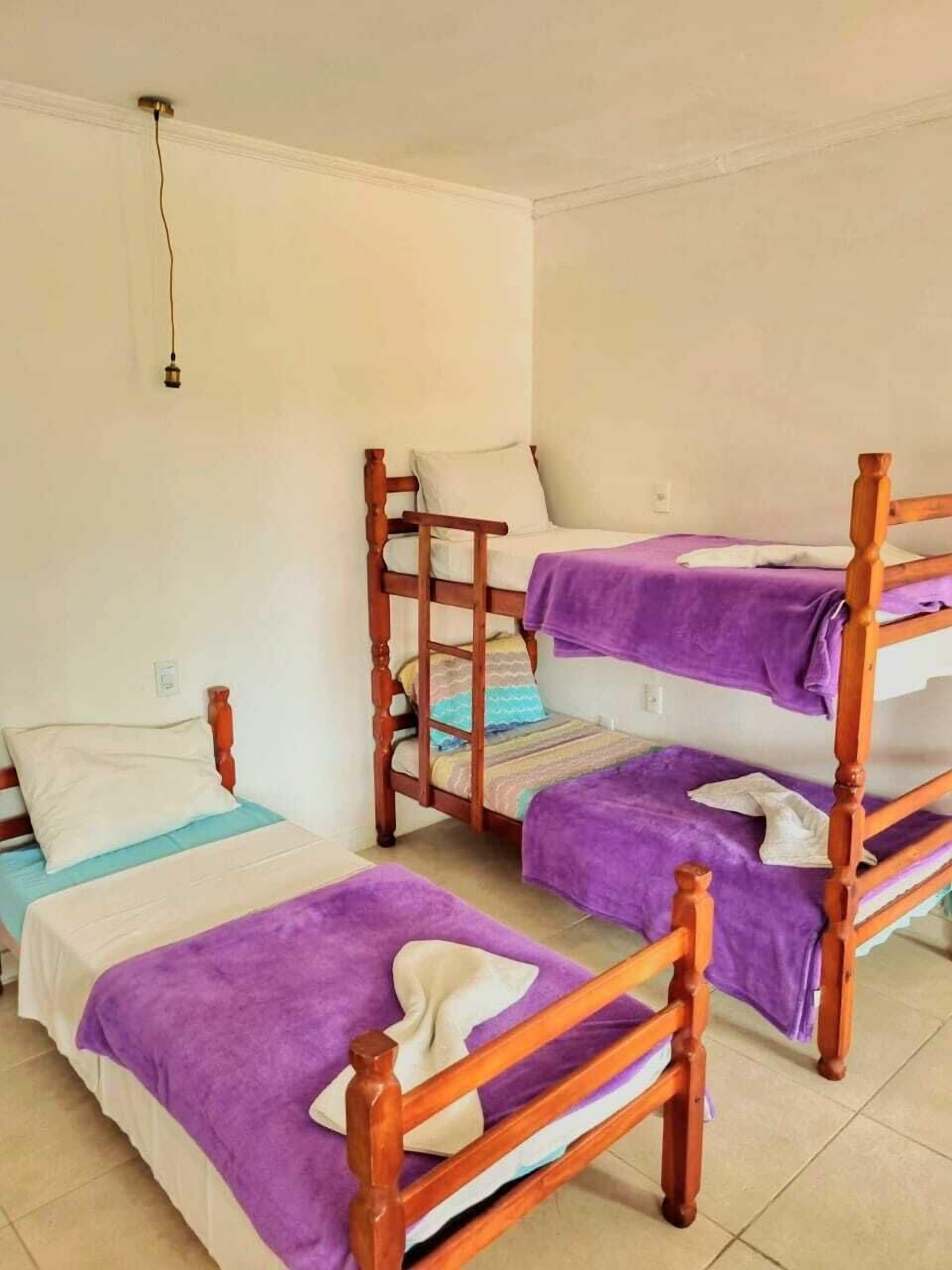 A dormitory room with bunk beds, each with a purple blanket and pillows.
