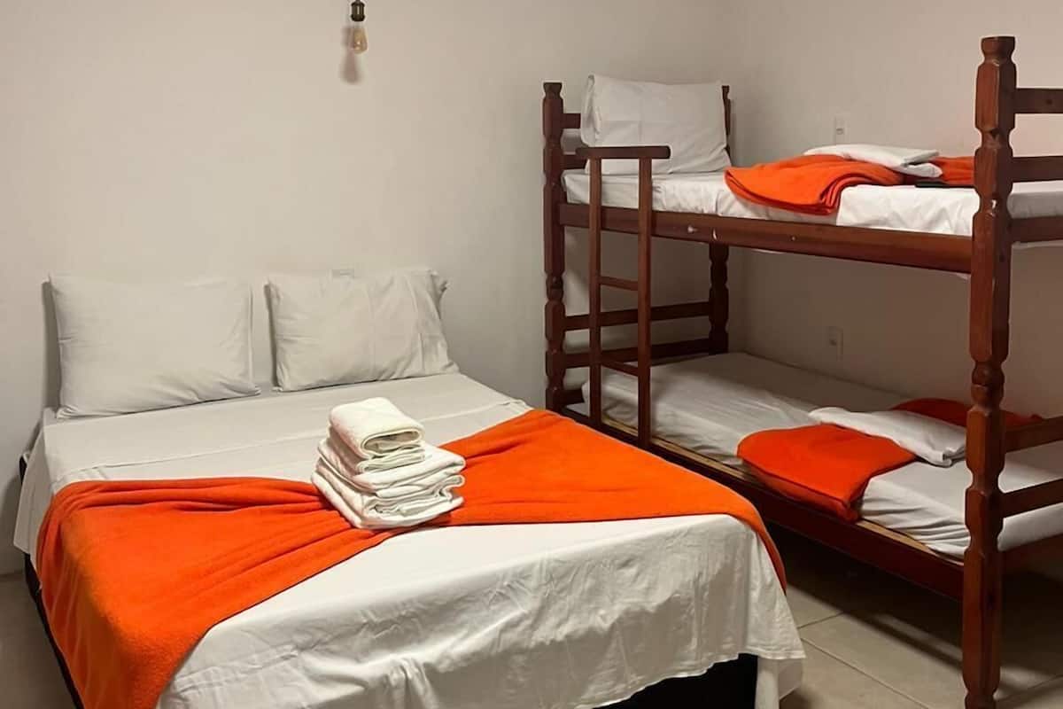 A dormitory room with two bunk beds, a single bed, white bedding, and an orange blanket.