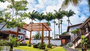 A residential area with a wooden pergola, palm trees, and a paved pathway. - Encanto dos Anjos (Búzios)