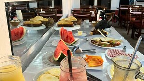A buffet table with various food items and drinks, including watermelon slices, sandwiches, and fruit. - Encanto dos Anjos (Búzios)