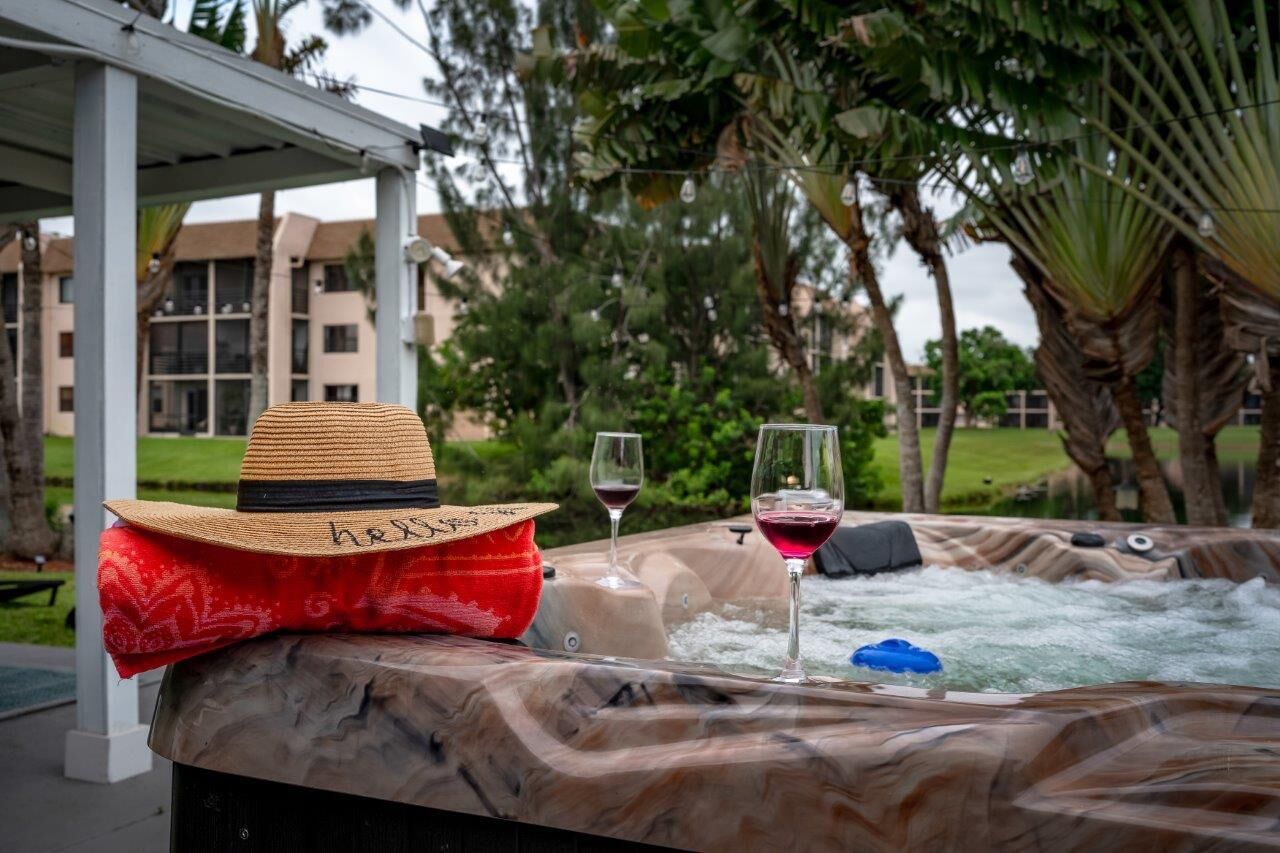 Un jacuzzi con sombrero de paja y tela roja, rodeado de árboles y un edificio al fondo.
