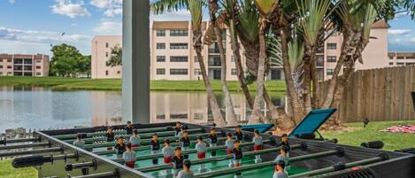 A foosball table set up outdoors with a view of a building and palm trees in the background.