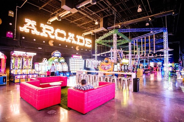 Eine Indoor-Spielhalle mit Neonreklame, Krabschere-Greifautomaten und einer großen Roboterfigur.