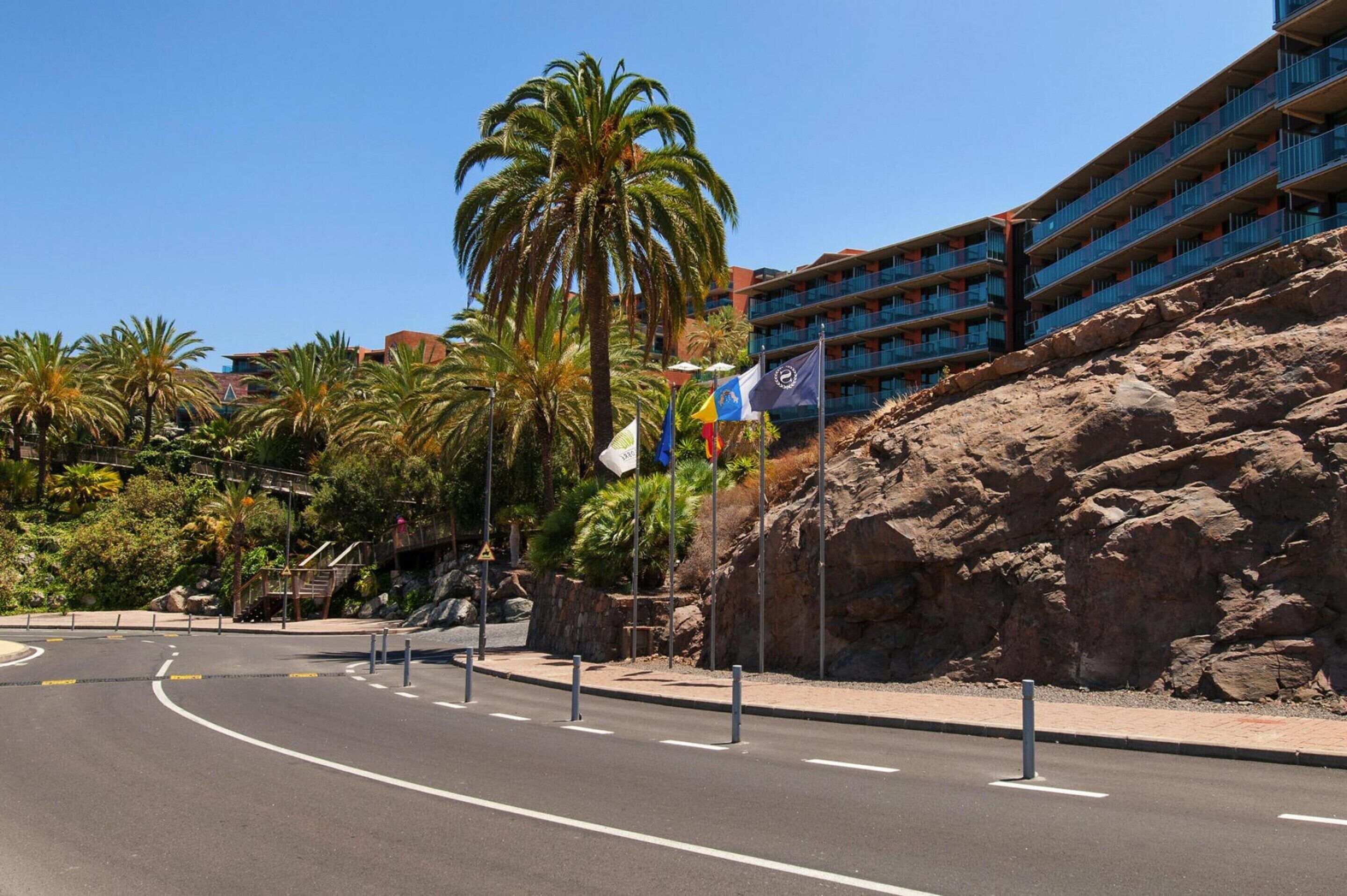 A hotel with multiple balconies, palm trees, and a rocky landscape.
