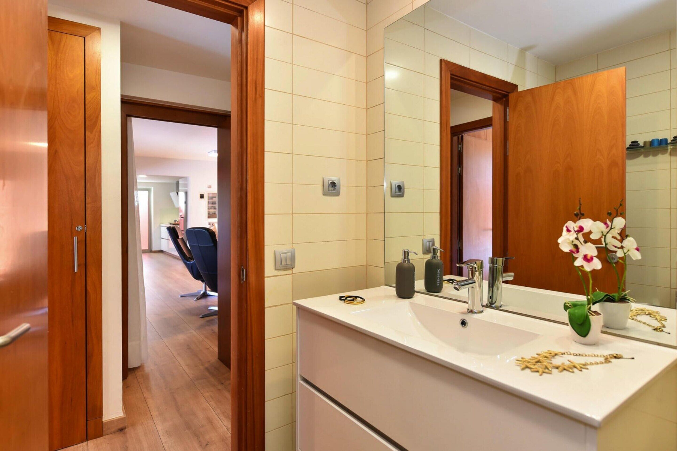 Une salle de bain moderne avec un grand miroir, un lavabo blanc et une porte en bois.