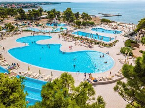 A large outdoor swimming pool complex with multiple pools and sunbathing areas, surrounded by trees and a view of the sea. - Apartment in Zaton-nin Near the sea (Nin)