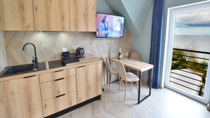 A modern kitchen with wooden cabinets, a black sink, and a dining area with a table and chairs. A television is mounted on the wall, and a balcony with a view of the sea is visible. - Apartment Right by the Sea, Ustronie Morskie (Ustronie Morskie)