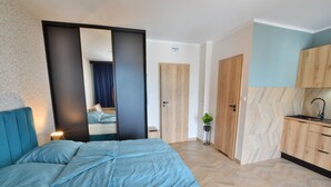 A bedroom with a bed, a mirror, a wardrobe, and a kitchenette. - Apartment Right by the Sea, Ustronie Morskie (Ustronie Morskie)