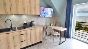 A modern kitchen with wooden cabinets, a built-in sink, and a dining area with a table and chairs. - Apartment Right by the Sea, Ustronie Morskie (Ustronie Morskie)