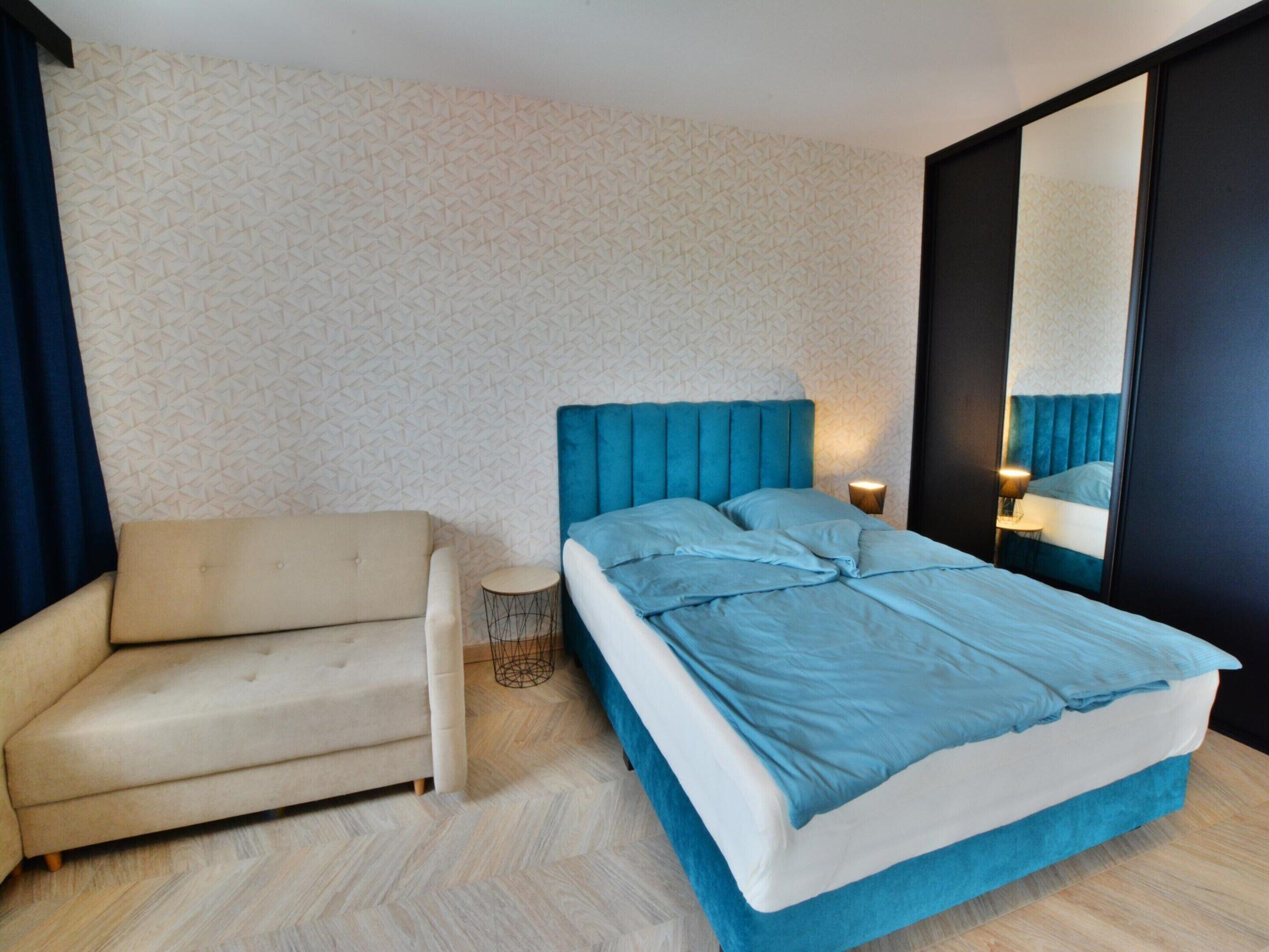 Ein modernes Schlafzimmer mit einem Bett, einem Sofa, einem kleinen runden Tisch und einem Spiegel.
