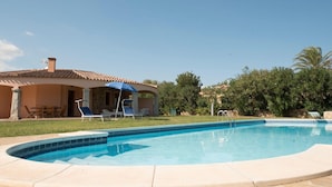 Area piscina con solarium in pietra, lettini e zona relax coperta.