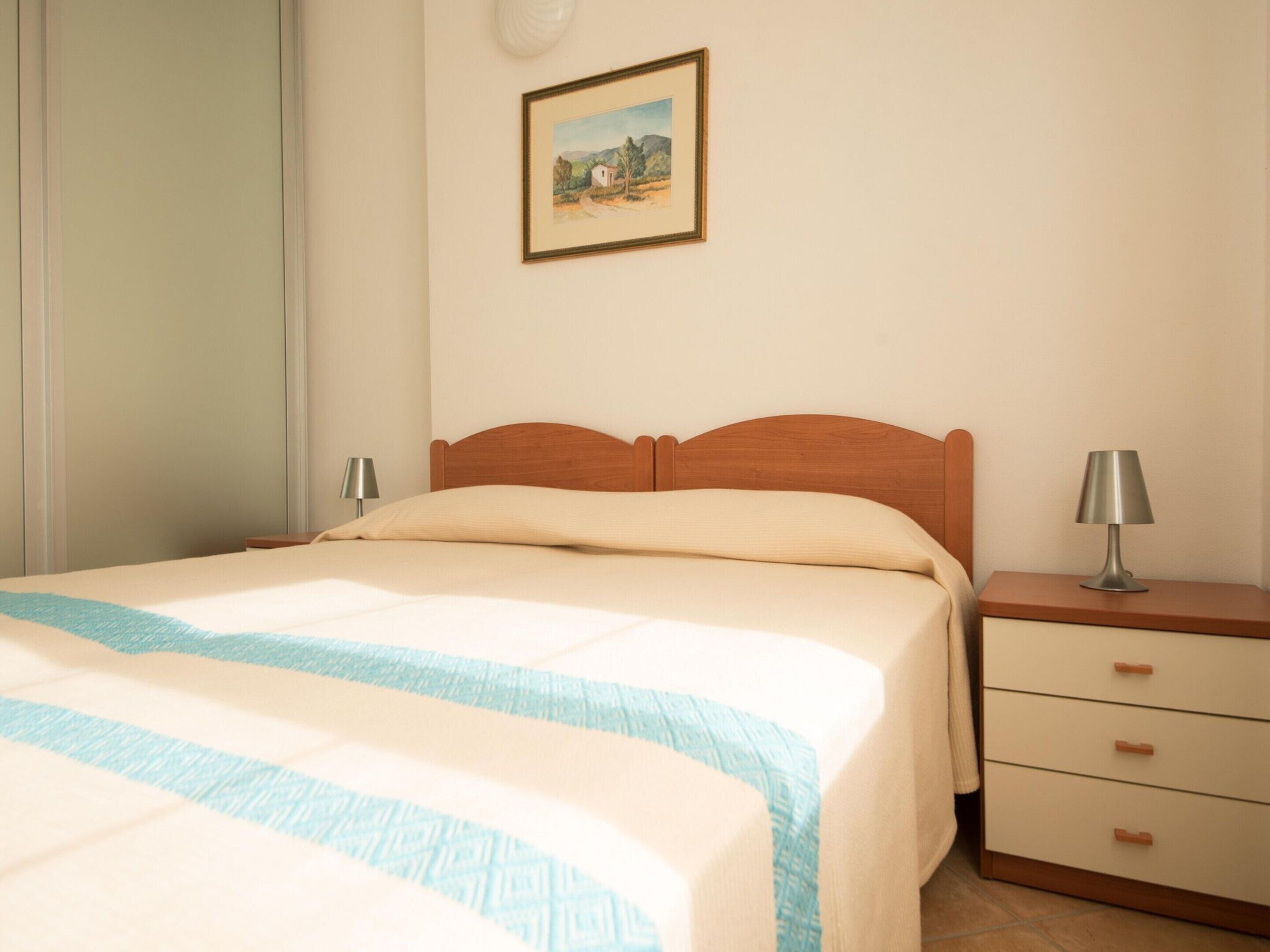A neatly made bed with a striped bedspread, a wooden headboard, and a bedside table with a lamp.