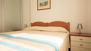 A neatly made bed with a striped bedspread, a wooden headboard, and a bedside table with a lamp.