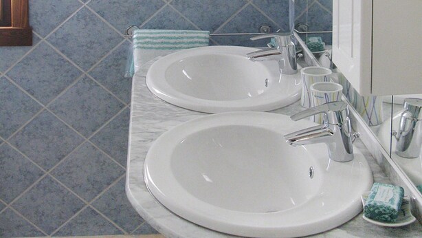 A bathroom with two sinks, a mirror, and blue and white tiled walls. - Villa in San Pietro Near White Sand Beach (Castiadas)