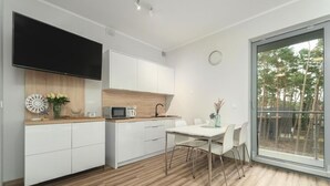 A modern kitchen with white cabinets, a microwave, and a dining area with a table and chairs. - Holiday Studio Very Close to the Seaside Beach (Rewal)